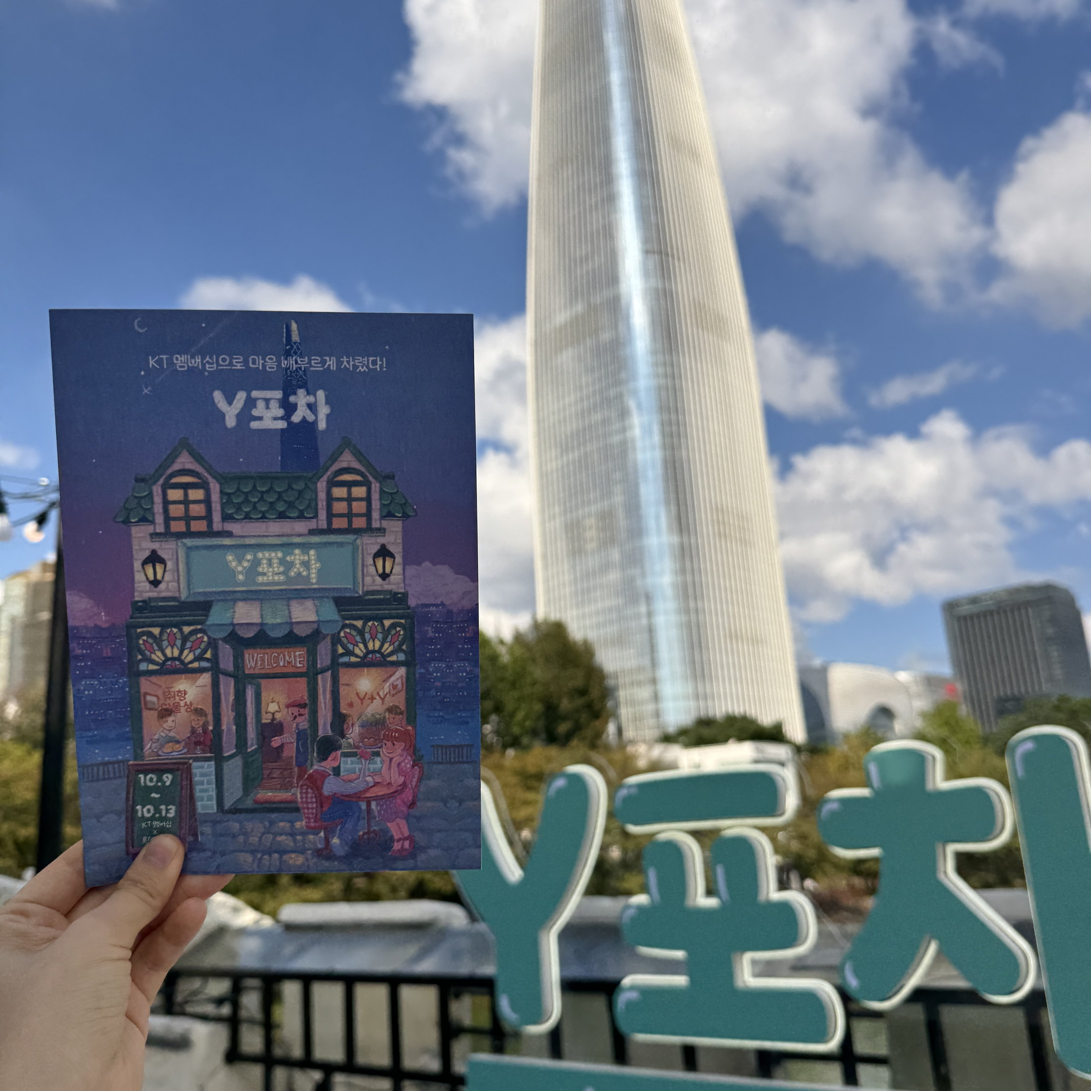 Printed Y Pocha key visual held in front of the pop-up space.